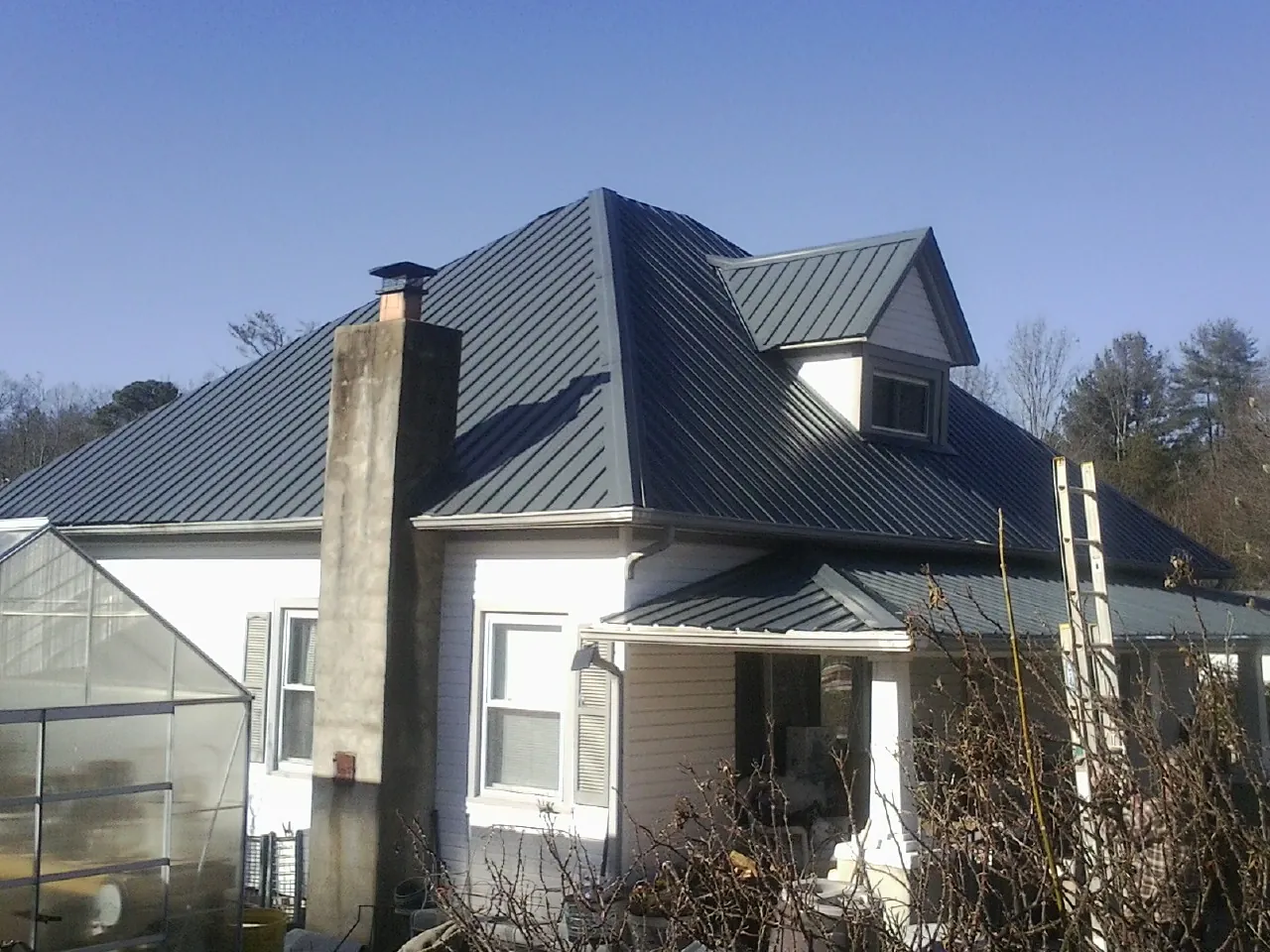 Dark blue standing seam metal roof on a white farmhouse with dormer — Slate & Tile Roof Repair by Roofing Brothers in Doswell