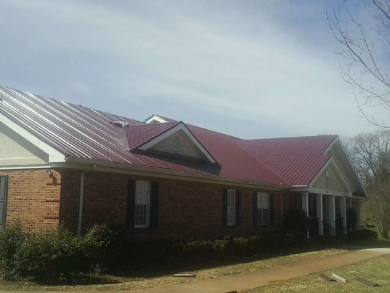 Red metal roof with gabled entries on a long brick building, from a Hail Damage Roof Repair job in Doswell