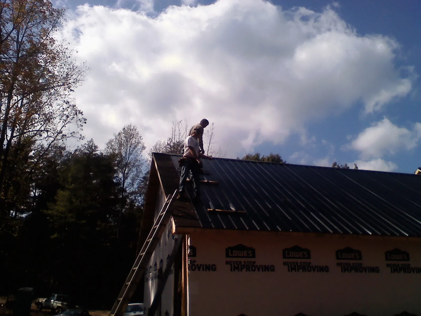 Roofer fastening dark metal panels high against a cloudy sky, from a Roof Inspection job in Doswell