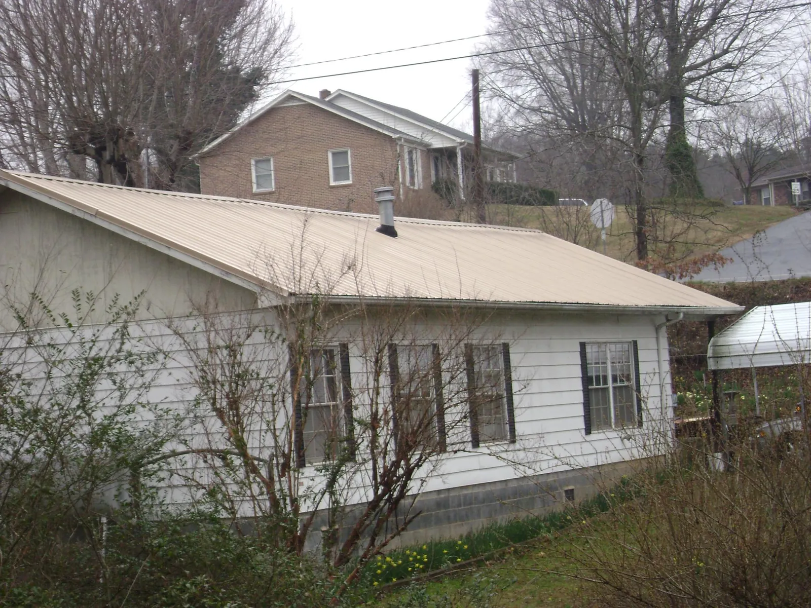 Tan metal roof on a white sided house set into a hillside — Commercial Roofing by Roofing Brothers in Doswell